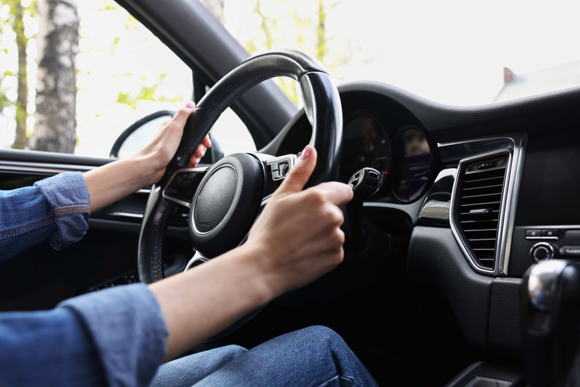 Hands gripping a black steering wheel inside a car, driving.