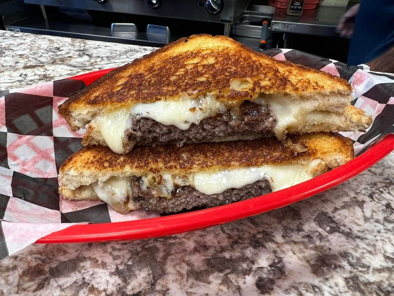 Grilled cheese sandwich with melted cheese and beef on a red plate, served in a diner-style setting