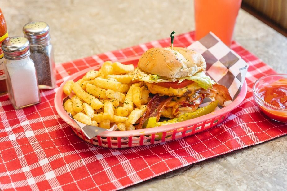 Burger and fries on a red checkered tray with condiments on a table