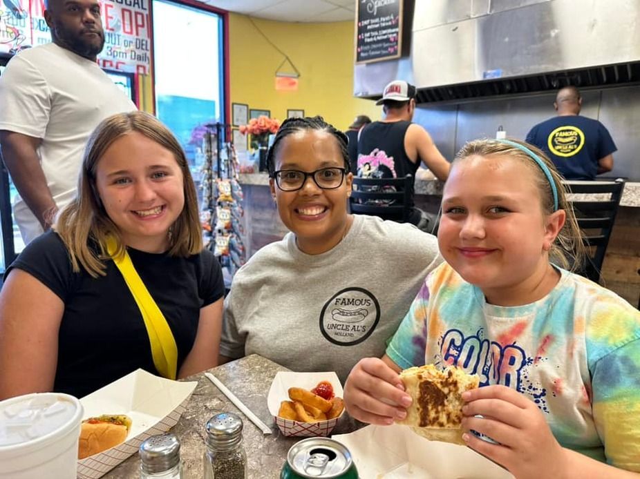 Three friends smiling at a restaurant table with plates of food and drinks
