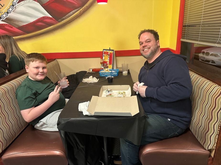 Two people seated at a restaurant table, smiling with cake and a gift box in front of them.
