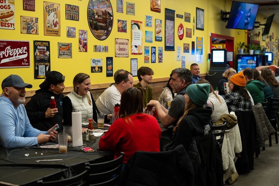 People seated at a long table in a colorful restaurant with yellow walls and framed artwork.