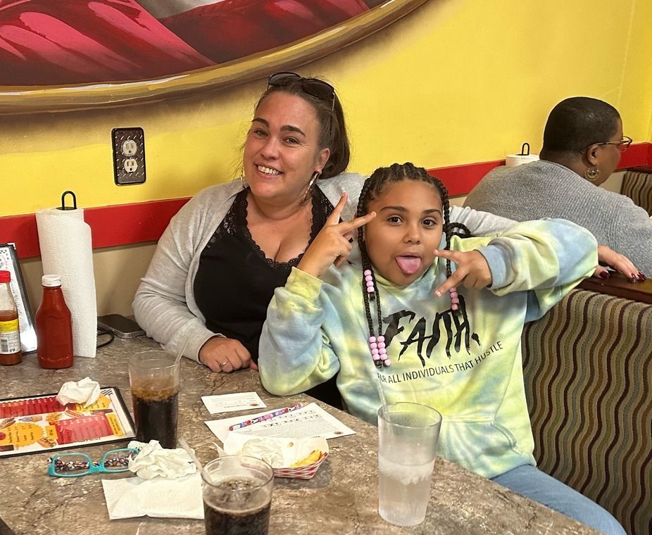 Two people smiling at a restaurant table with drinks and plates, posing with peace signs