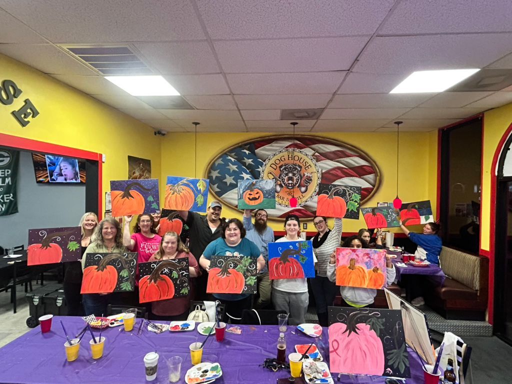 Group seated in a classroom holding colorful paper pumpkins and drawings with orange and purple Halloween decorations