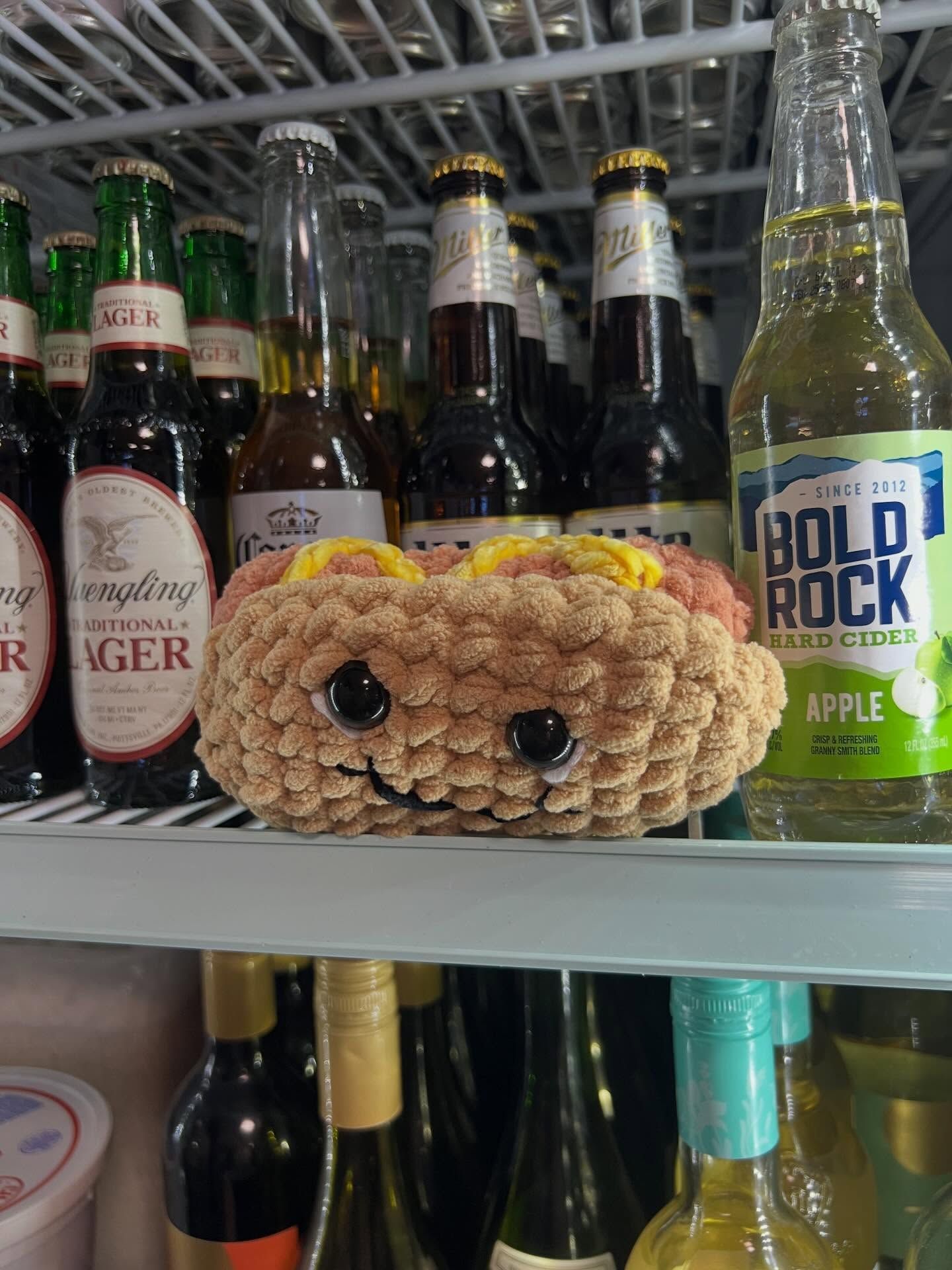 A crocheted cat-shaped cozy on a store shelf among beer bottles and a green Bold Rock cider bottle