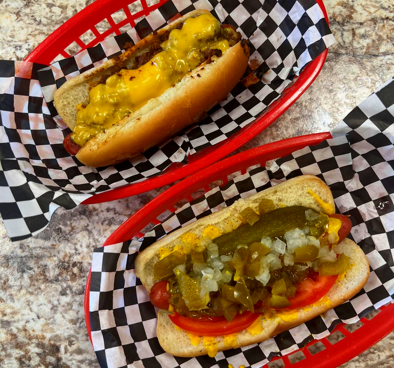 Two Chicago-style hot dogs in red baskets with checkered paper, topped with relish and peppers