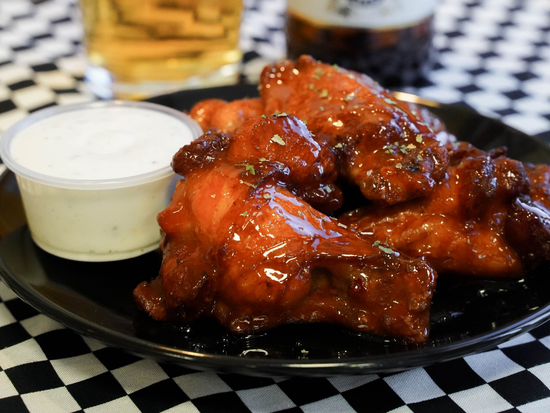 Glazed chicken wings on a black plate with a cup of dipping sauce on a checkered tablecloth