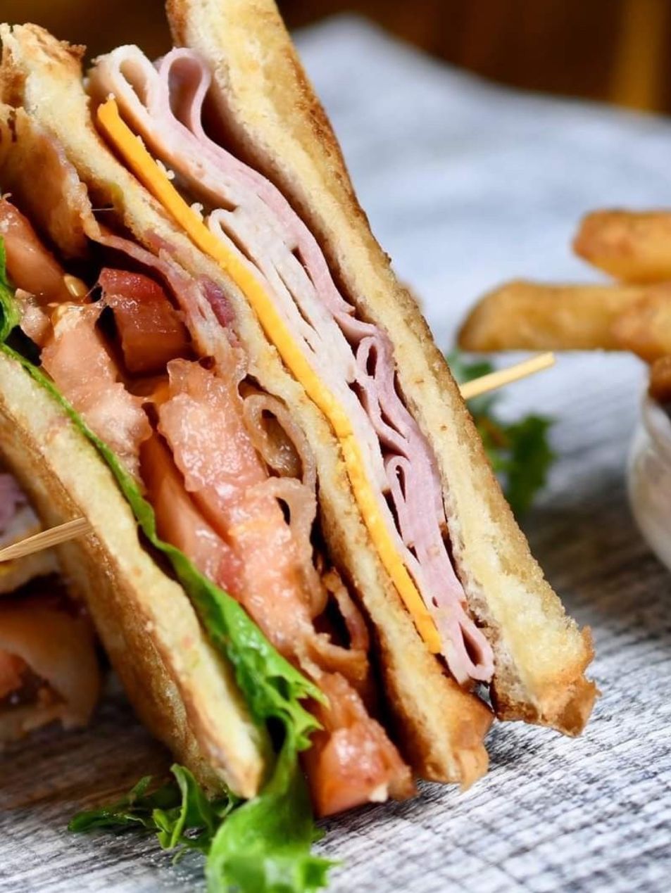 Close-up of a stacked sandwich with ham, cheese, turkey, lettuce, and tomato on toasted bread
