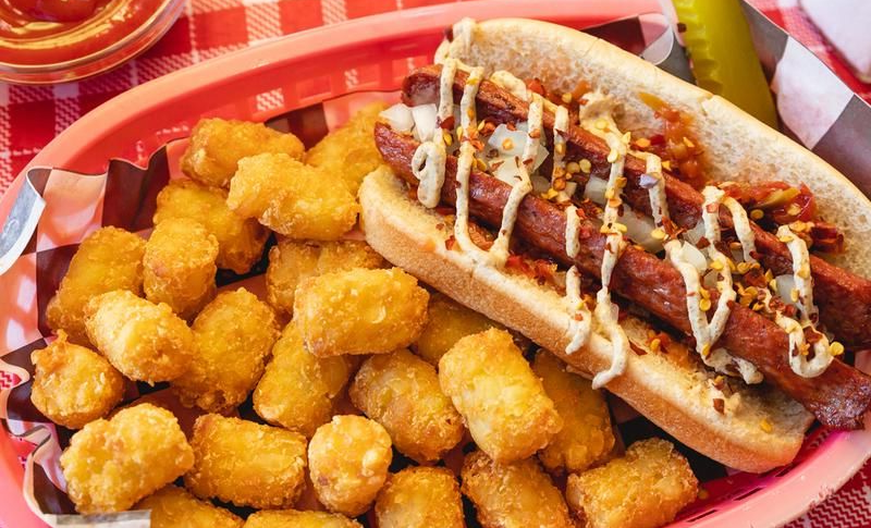 Tater tots and a hot dog topped with sauerkraut, mustard, and diced onions on a pink tray