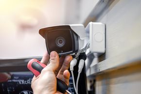A man installing a security camera on a wall.