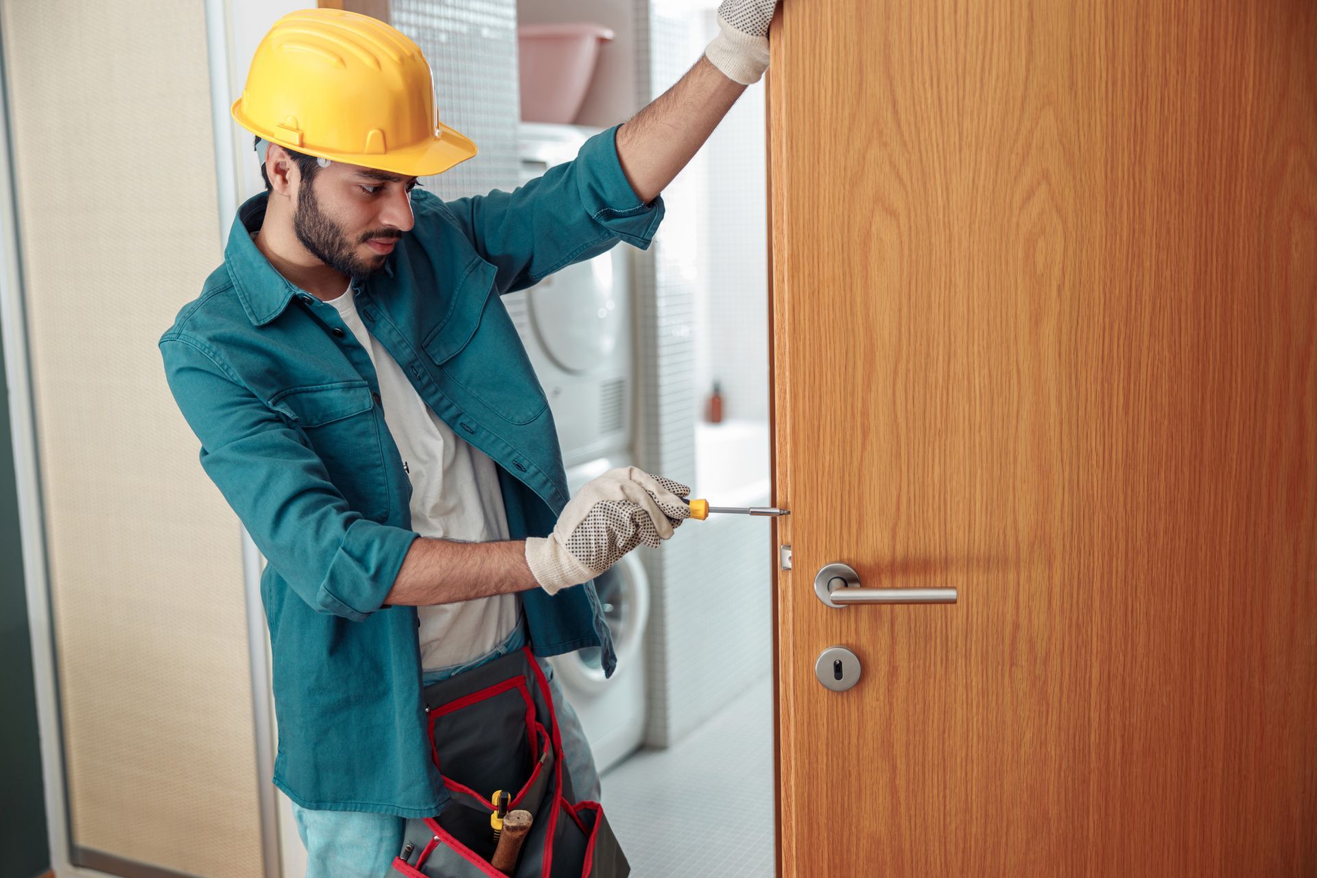 Worker in hard hat fixing a door with a screwdriver.