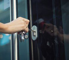 A man unlocking a glass door of an office with a key.