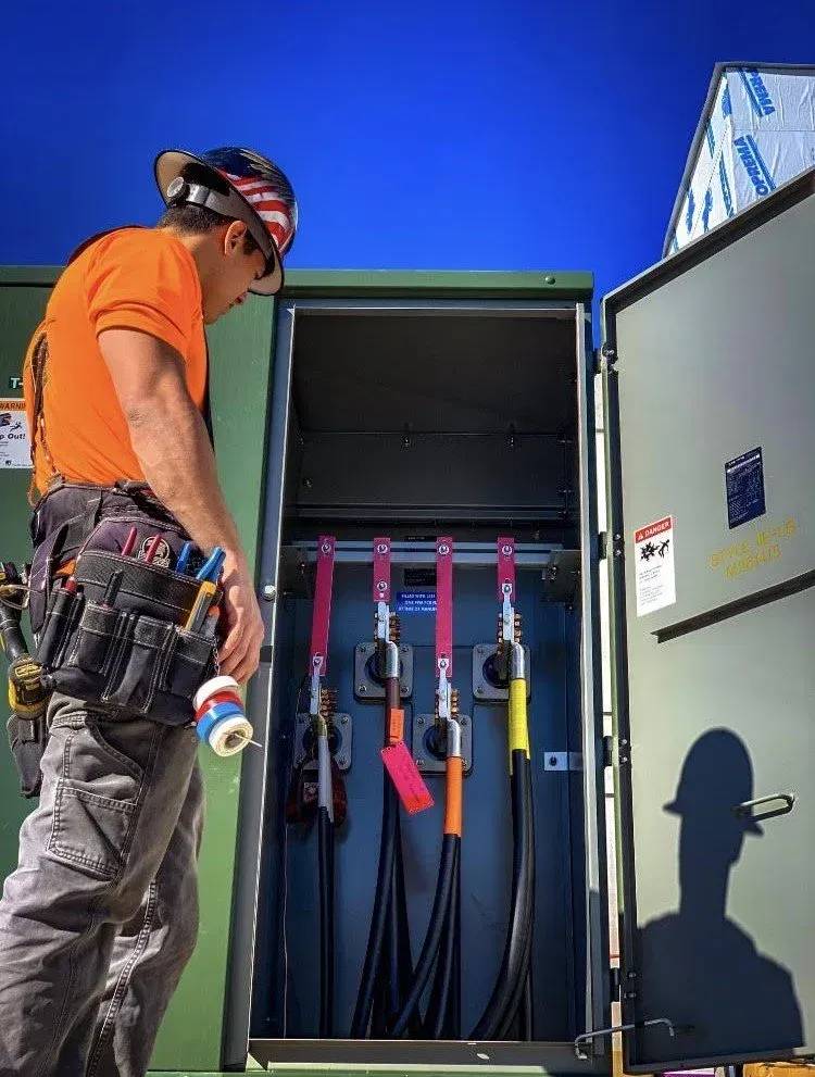 Technician inspecting an open electrical cabinet with cables and tools against a blue background