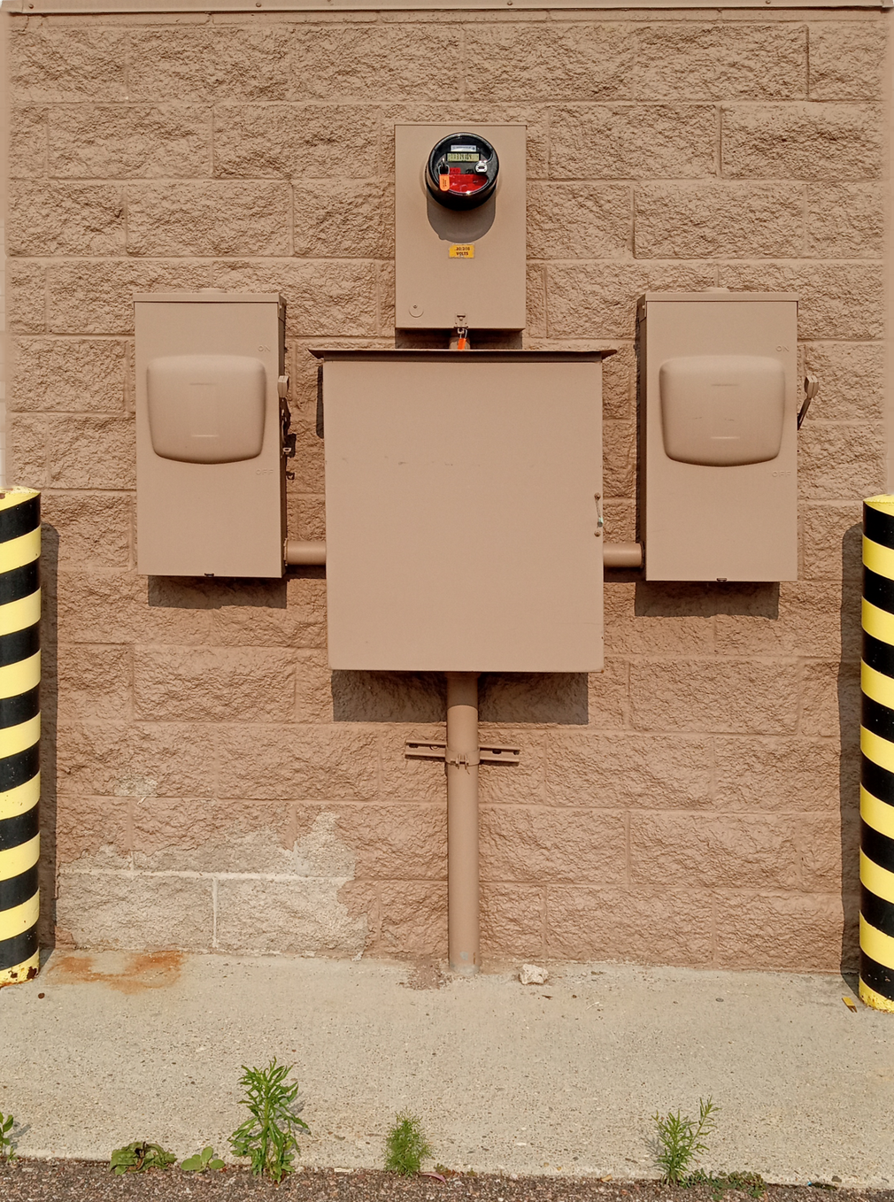 Wall-mounted electrical control boxes on a tan stucco wall with a red alarm light above.