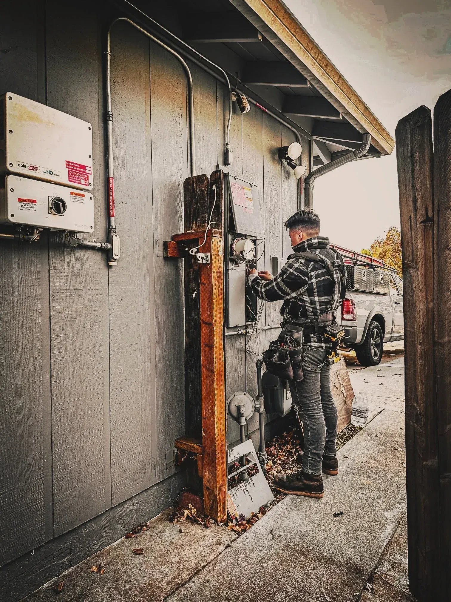 Worker inspecting electrical equipment beside a building, with a utility truck parked nearby.