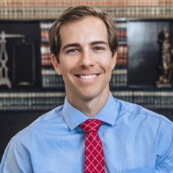 Man in blue shirt and red tie smiling in an office setting.
