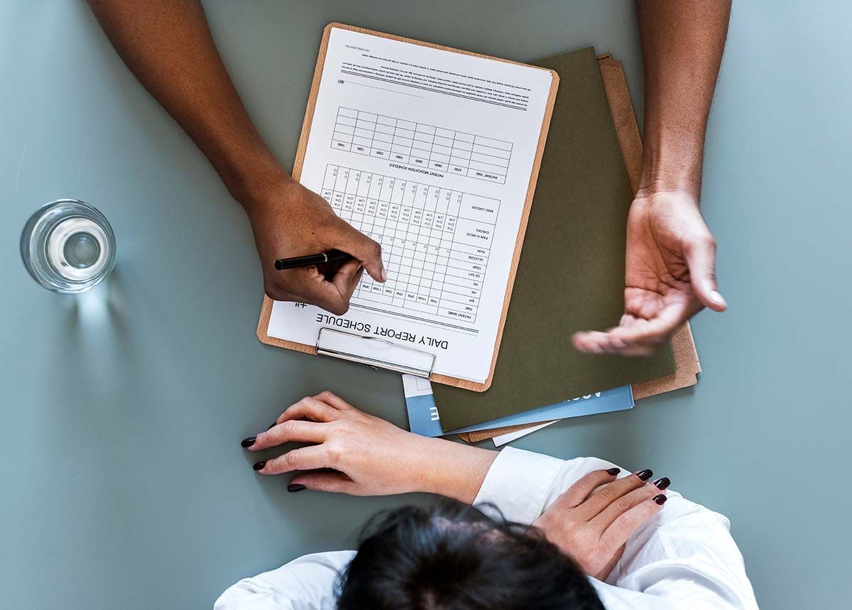 Two people reviewing a clipboard at a table with a measuring tape and a cup of coffee