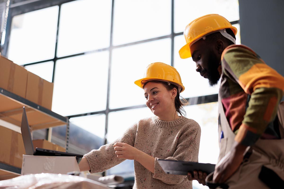 Two workers in yellow hard hats reviewing plans at a construction site