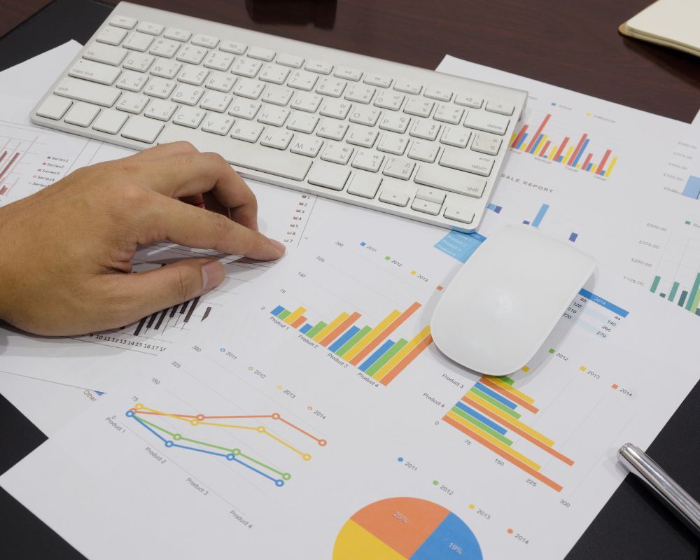 pointing at graphs on paper, near keyboard