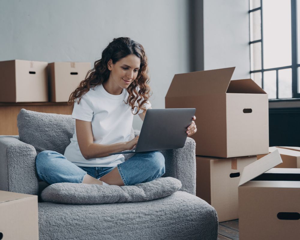 tenant using laptop on couch, surrounded by moving boxes