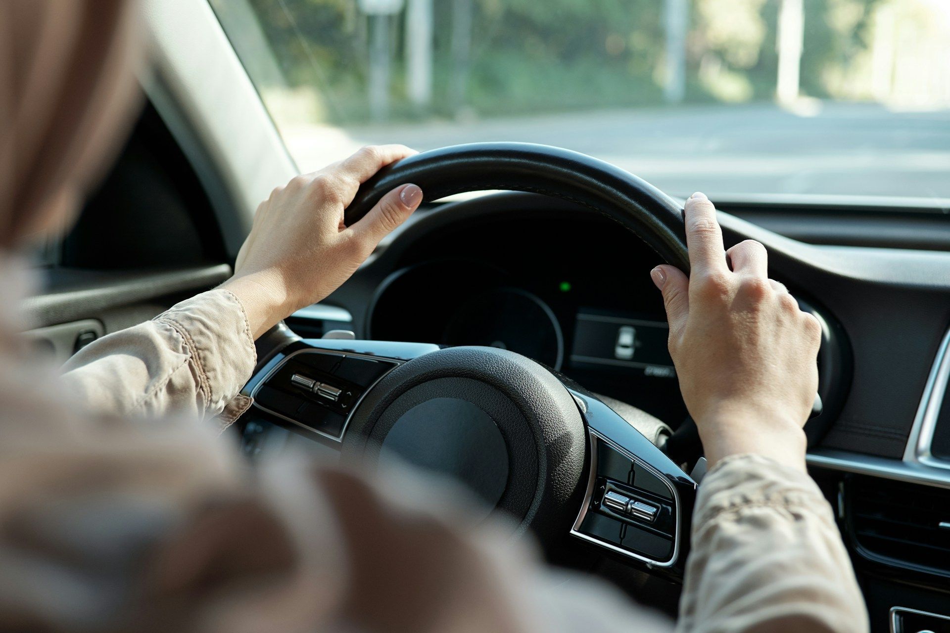 A person drives a vehicle, holding the steering wheel with both hands, viewed from the driver's perspective.