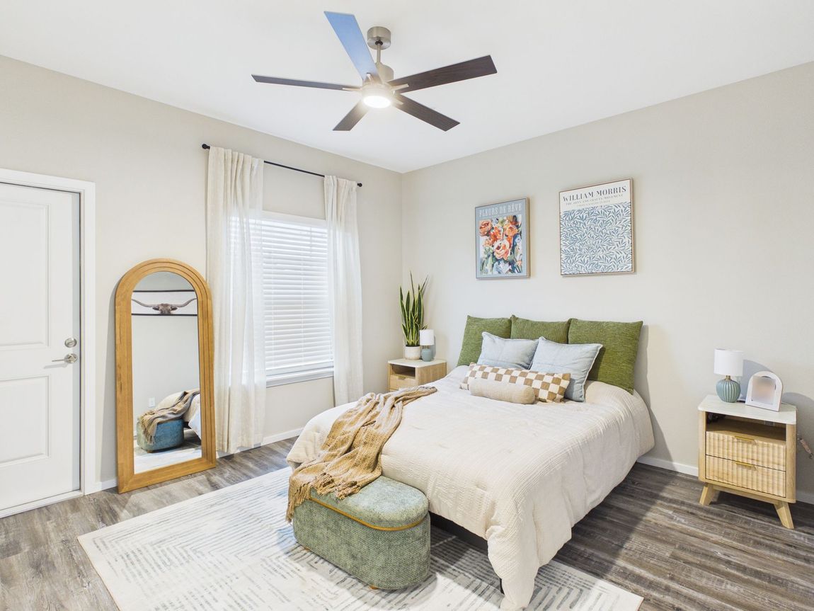 Bedroom with a wooden headboard, coral bedding, and a large potted plant. Two abstract art prints hang above the bed.