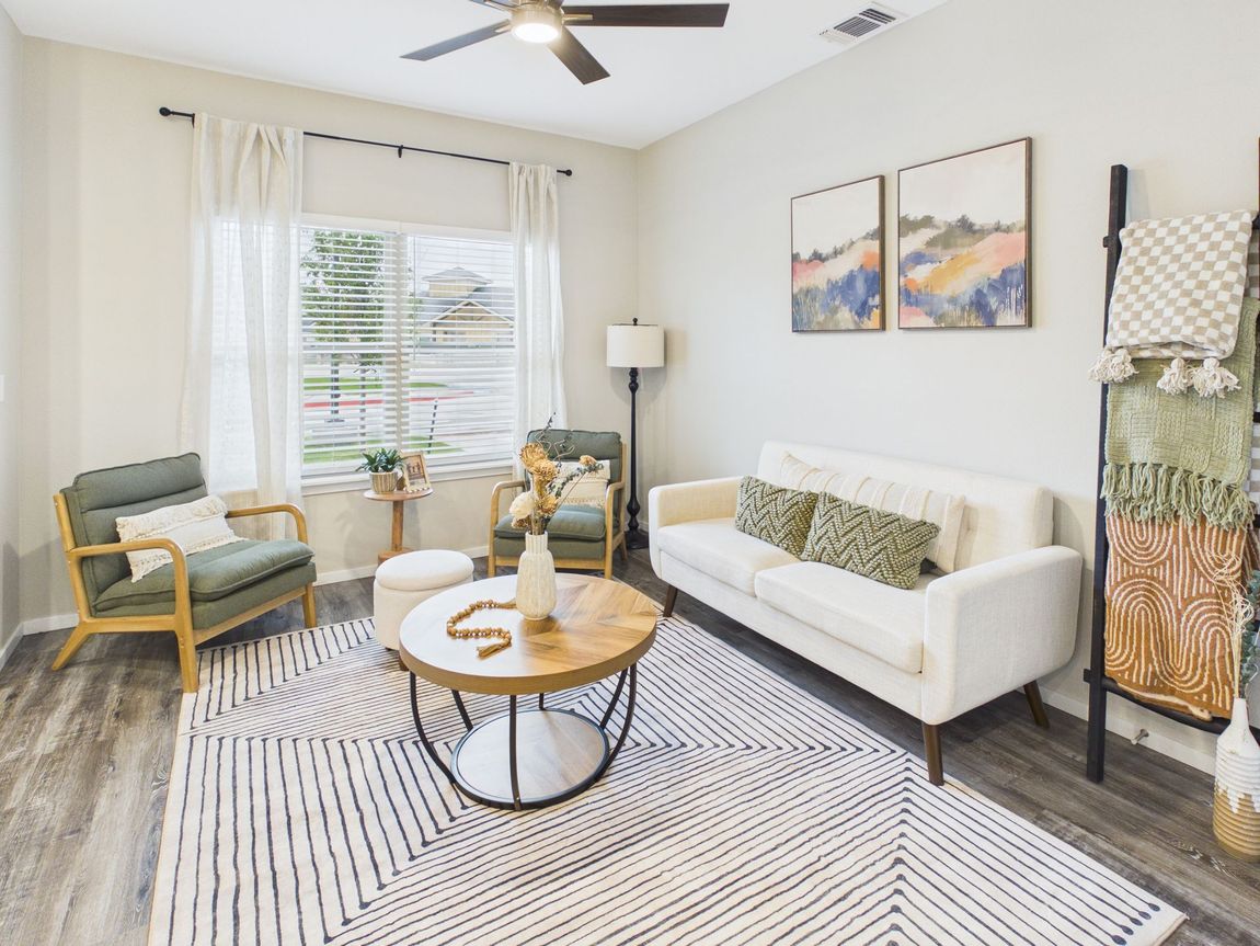 Living room with white sofa, rug, and wooden coffee table; neutral color scheme, plants, door on right.