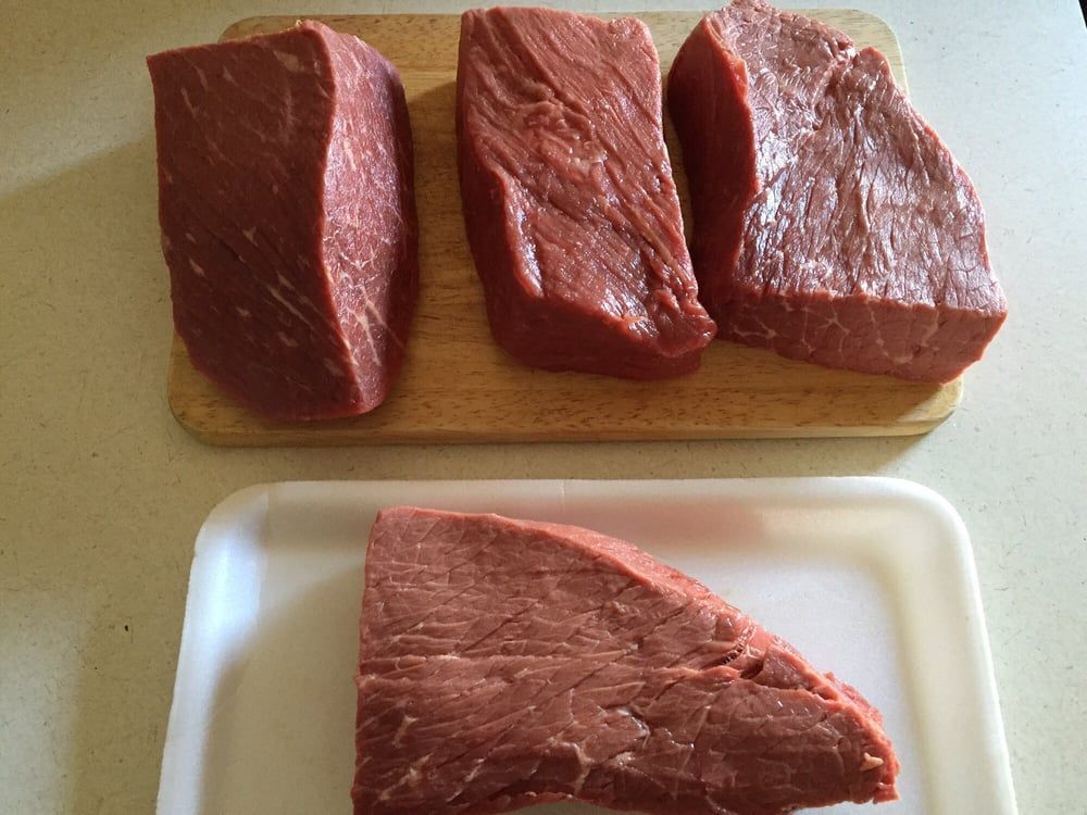 Raw red meat cuts on a cutting board and tray, arranged in two rows.
