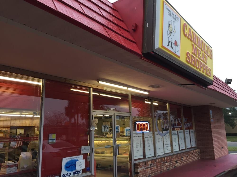 Strip mall storefront with red awning and yellow sign, lit window displays, and an open neon “OPEN” sign.
