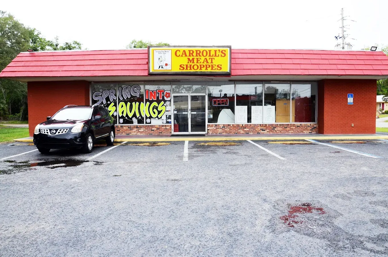 Small red restaurant storefront with a black car parked outside on a wet lot