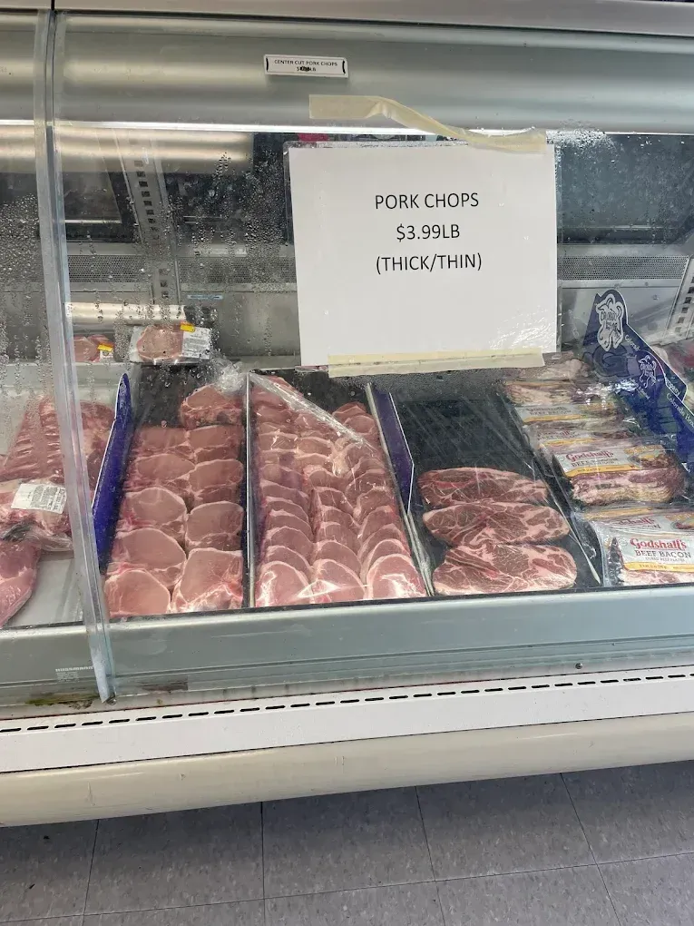 Butcher case with trays of raw meat and a handwritten sign in a refrigerated store display.