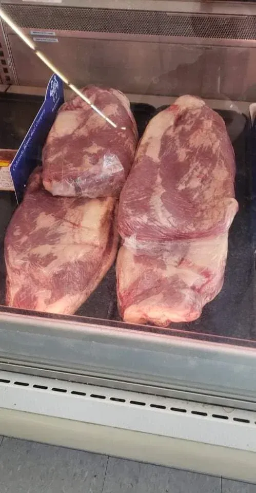 Four slabs of raw meat displayed in a refrigerated deli case.