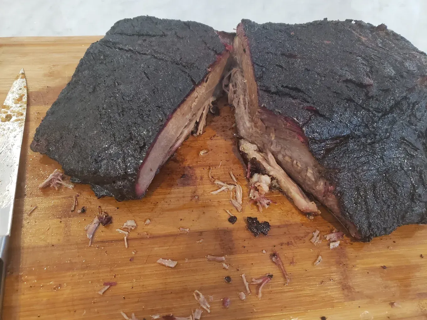 Smoked meat brisket sliced on a wooden cutting board with a knife beside it