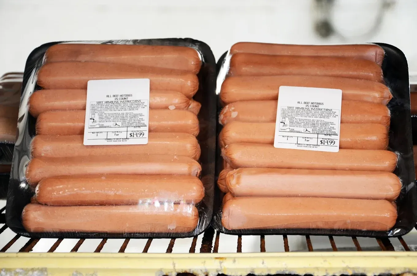 Two trays of packaged hot dogs in clear plastic wrapping on a store shelf
