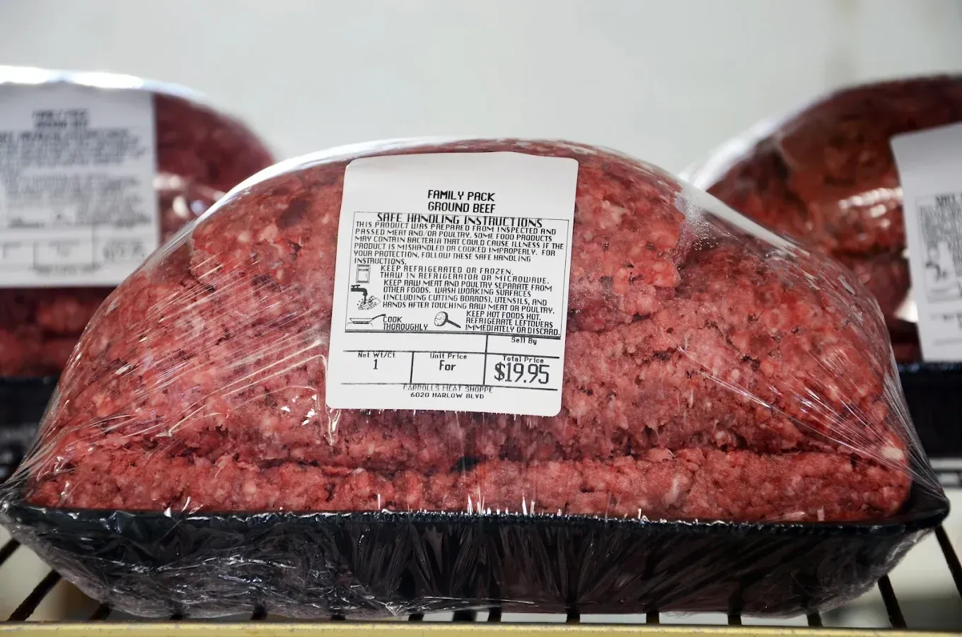 Packaged ground beef in black trays on a store shelf, with a white label on top.
