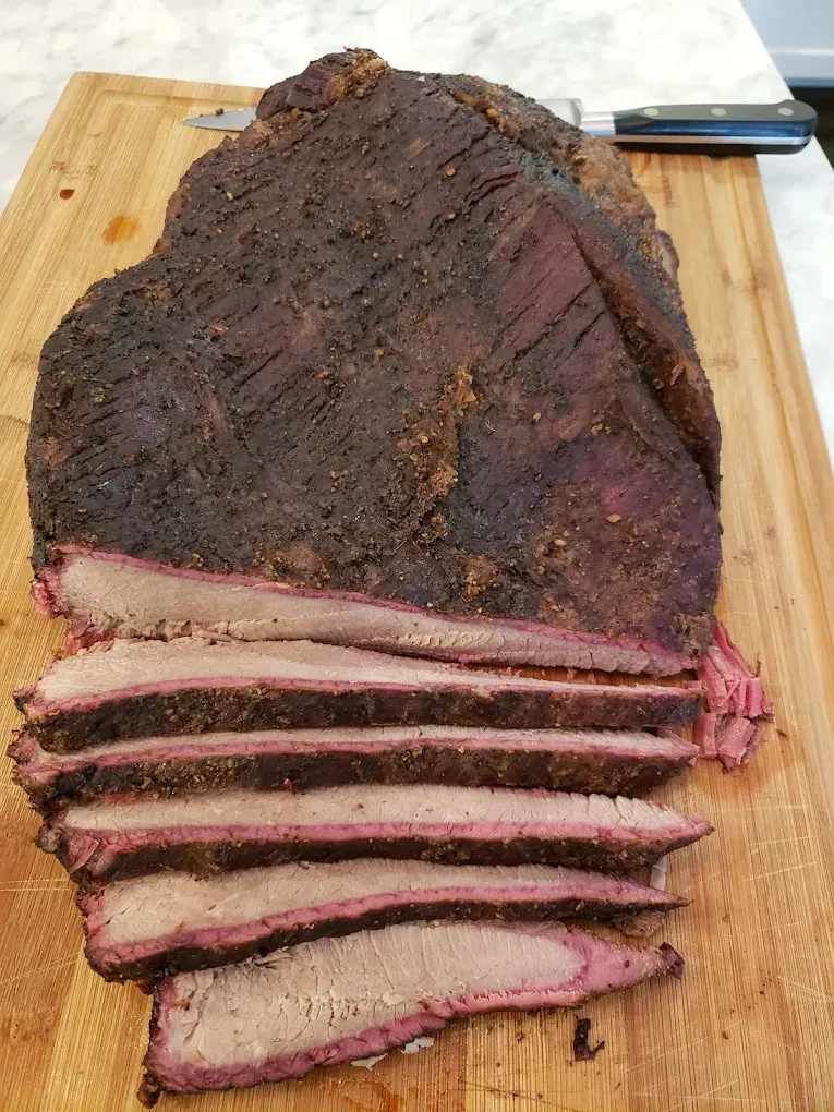 Sliced smoked brisket on a wooden cutting board with a knife in the background