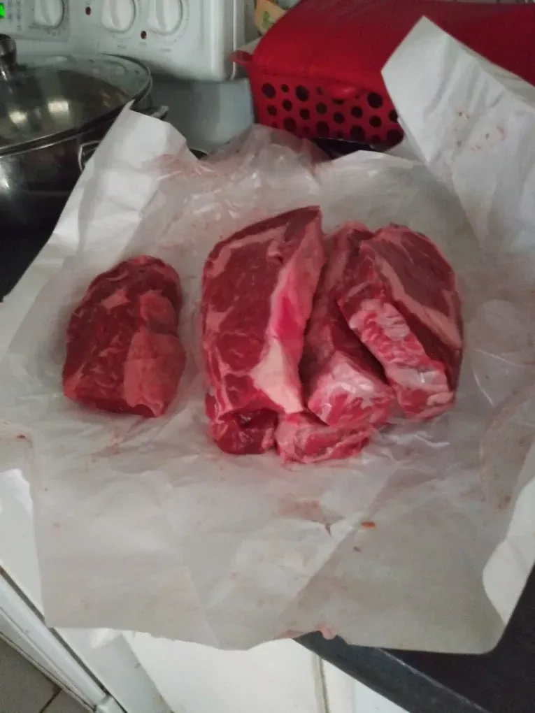 Three raw beef cuts on wax paper in a kitchen sink area