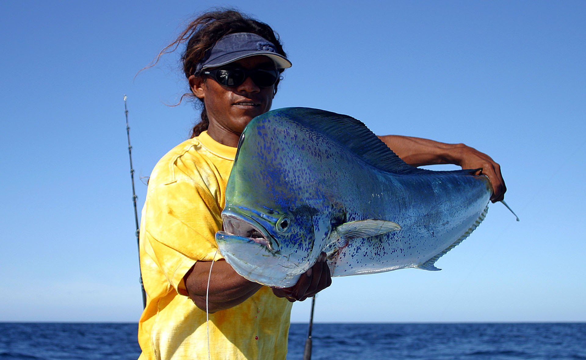 A man in a yellow shirt is holding a large fish