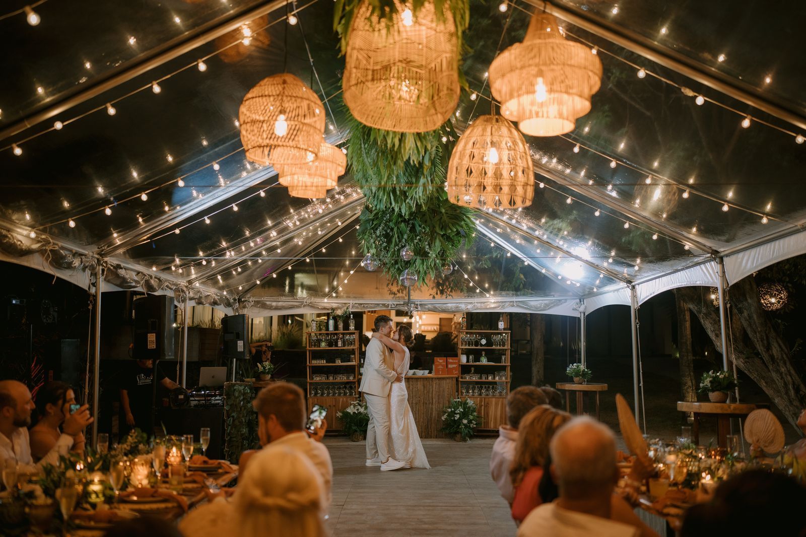 A bride and groom are dancing under a clear tent at their wedding reception.