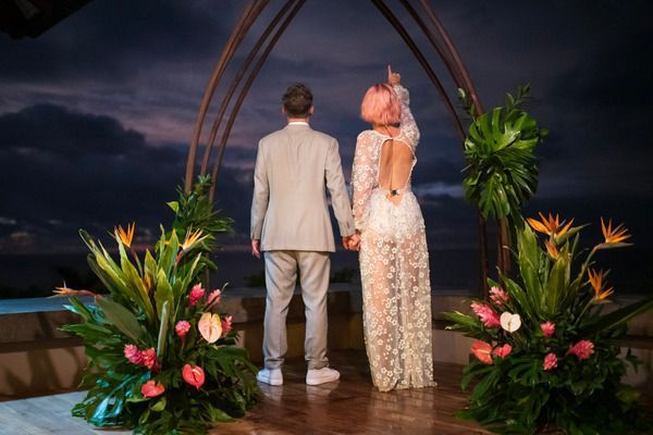 A bride and groom are standing in front of a wedding arch holding hands.