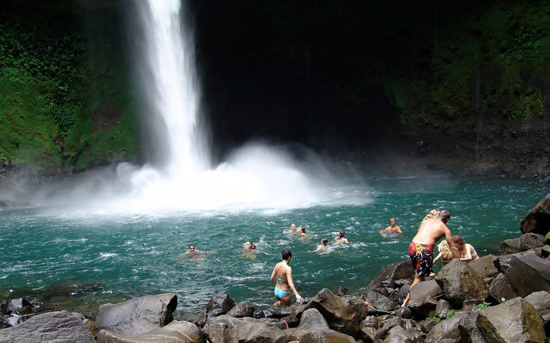 A group of people are swimming in a waterfall.