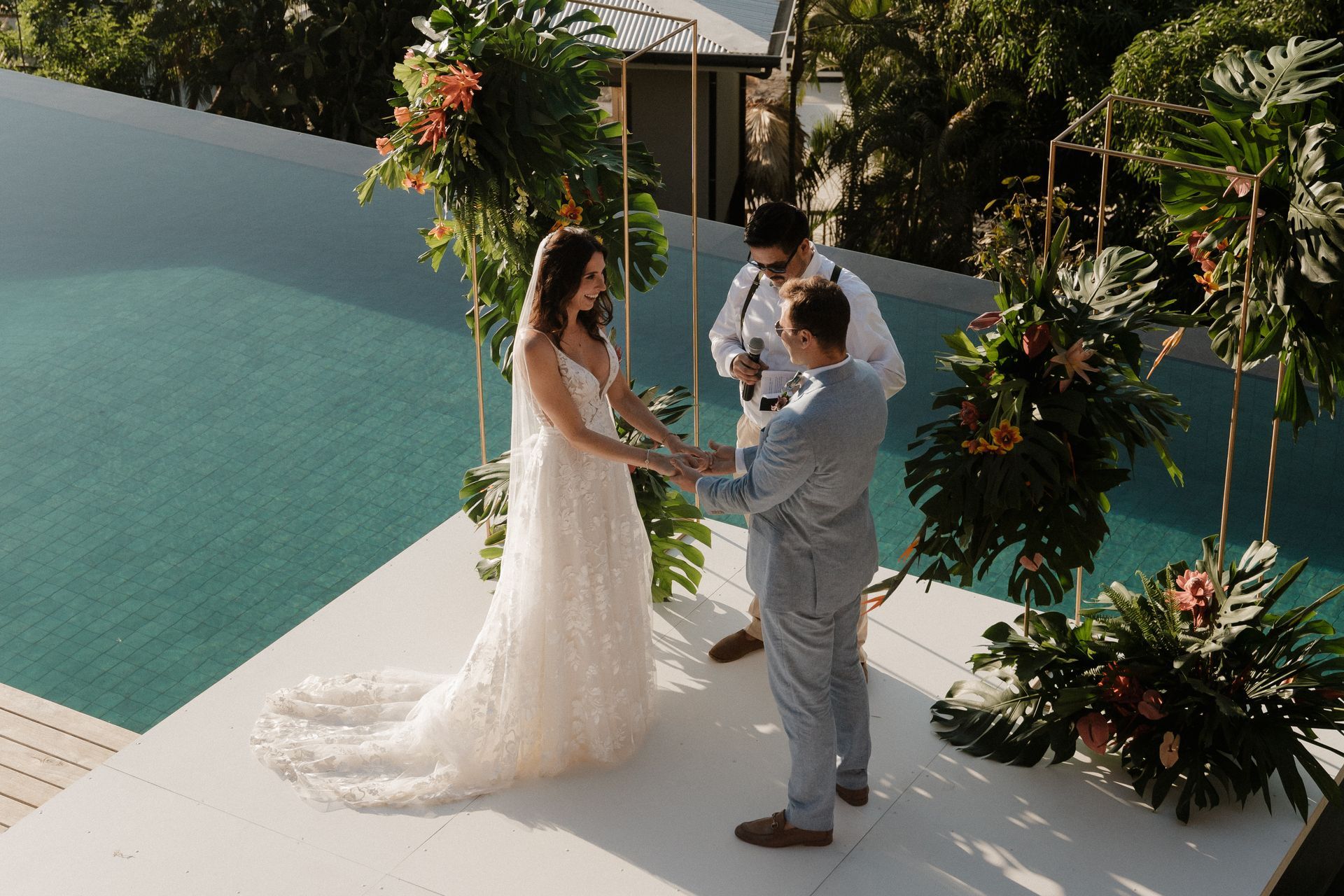 A bride and groom are holding hands during their wedding ceremony in front of a swimming pool.