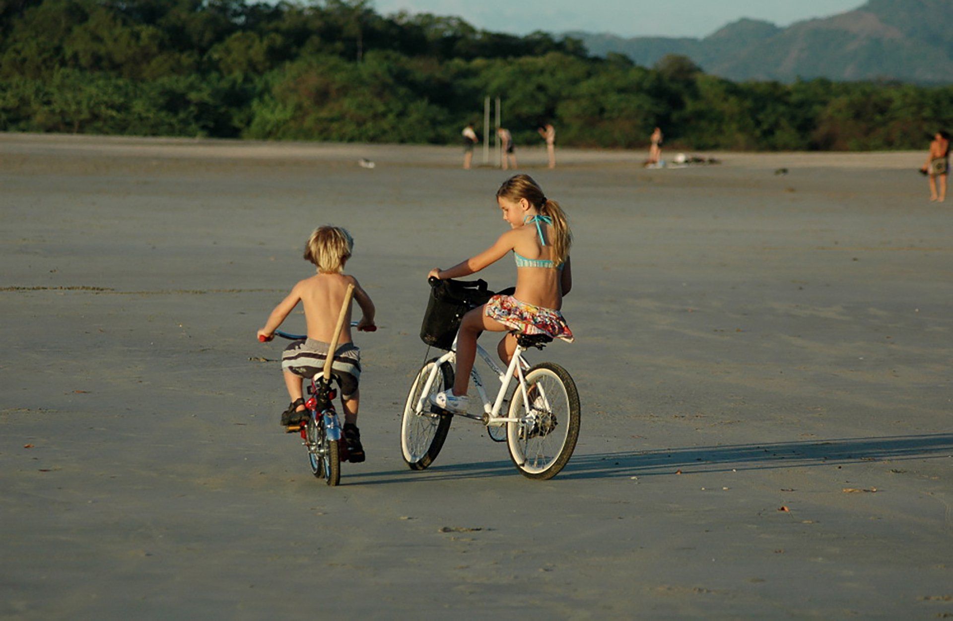 A boy and a girl are riding bicycles on the beach.
