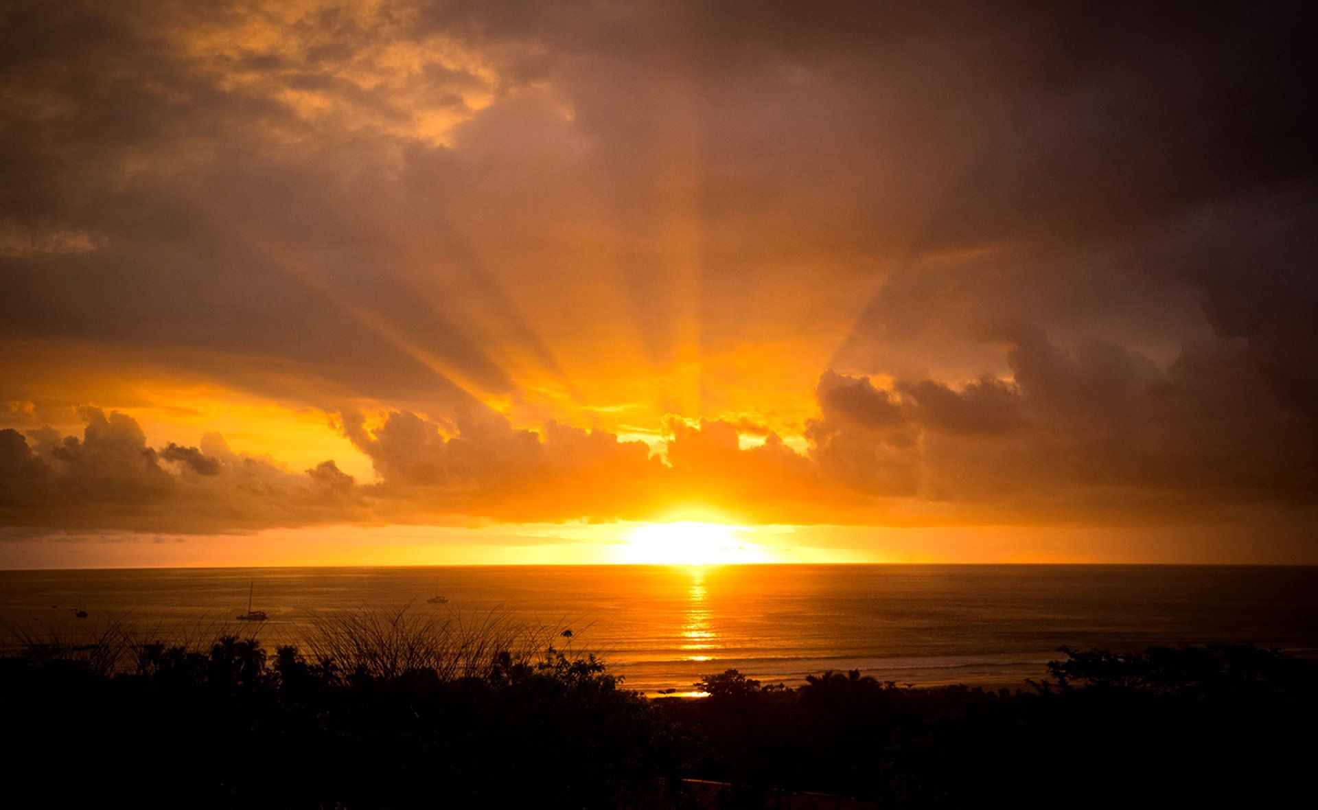 A sunset over the ocean with the sun shining through the clouds.