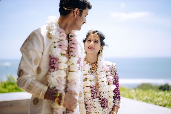 A bride and groom are standing next to each other wearing garlands of flowers.