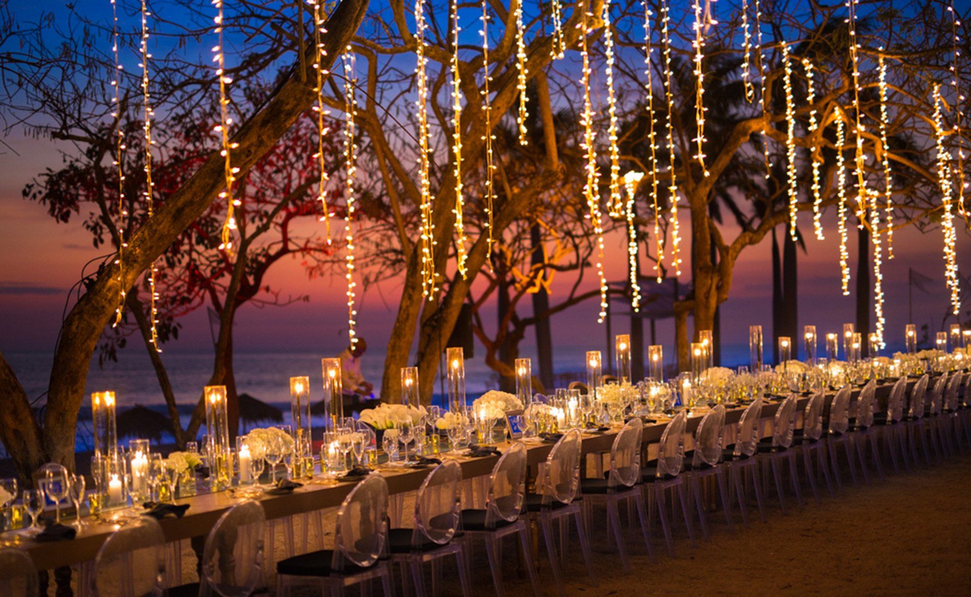 A long table with candles and lights hanging from the trees.