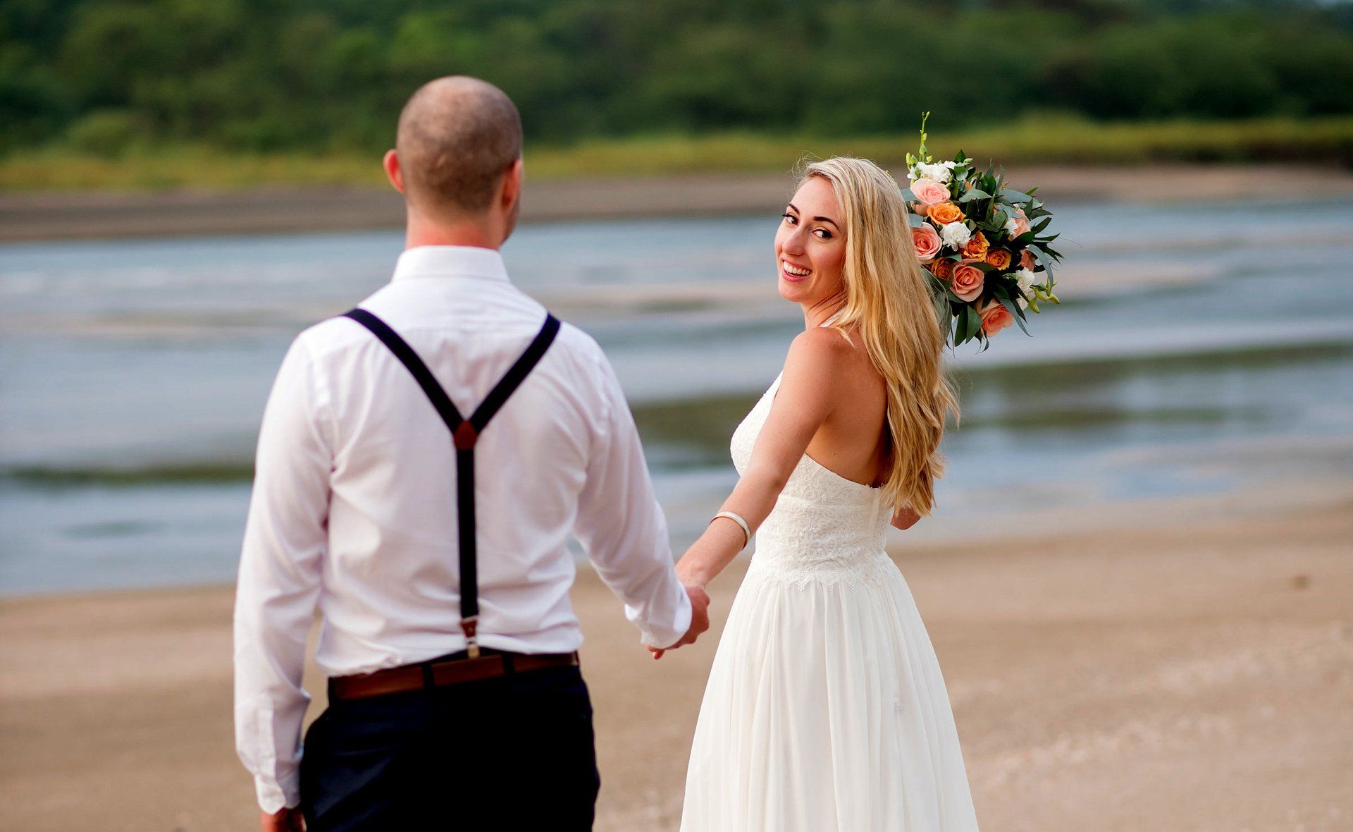 A bride and groom are holding hands on the beach.
