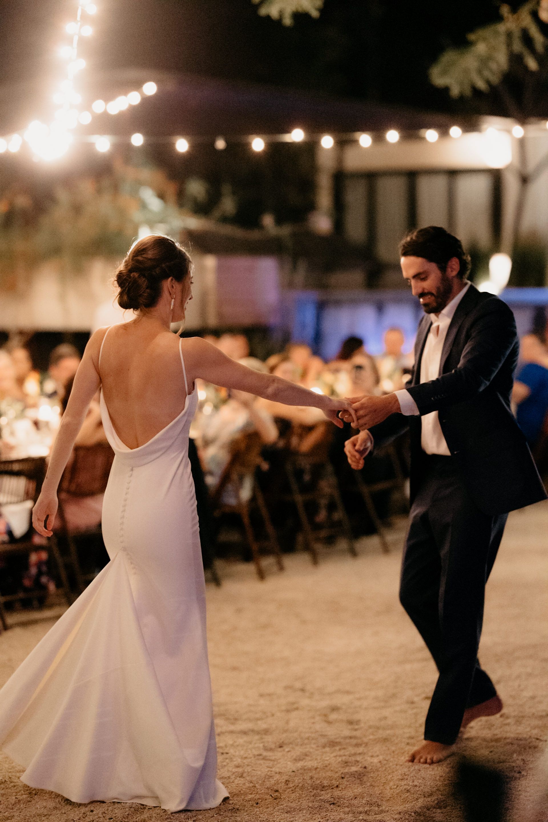 A bride and groom are dancing on the beach at their wedding reception.