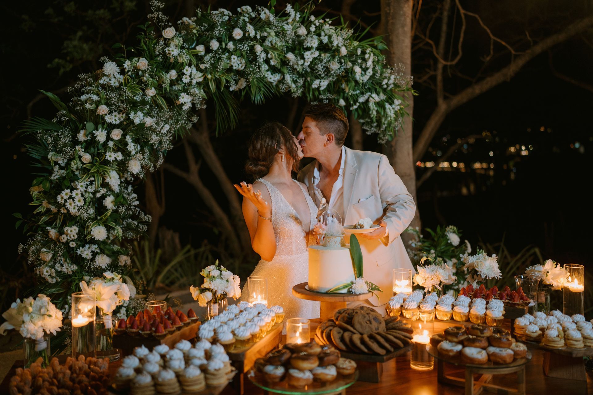 A bride and groom are kissing while cutting their wedding cake.