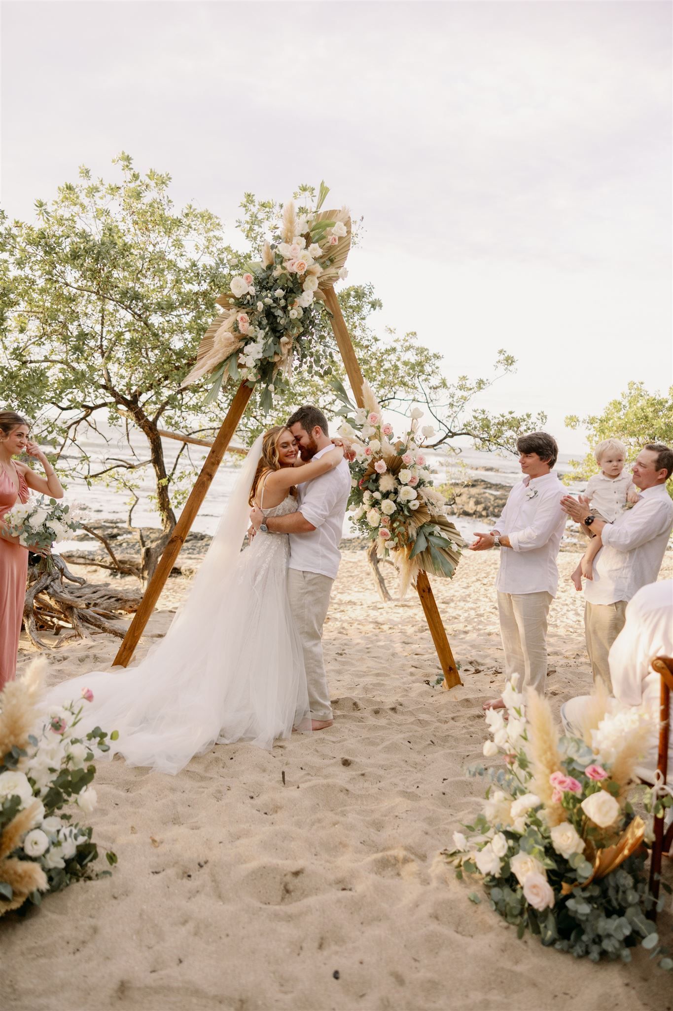 A bride and groom are hugging during their wedding ceremony on the beach.